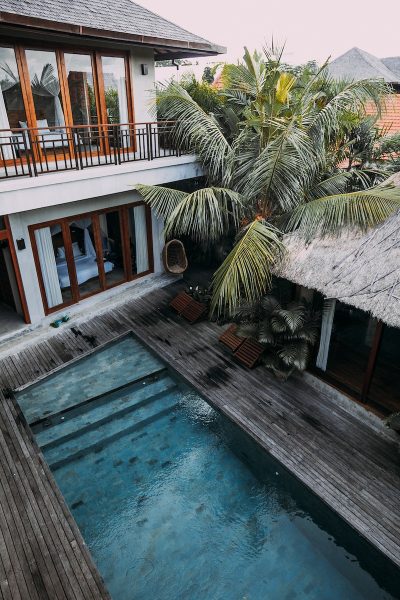 From above of wooden cottage with balcony located among tropical exotic trees with blue pool