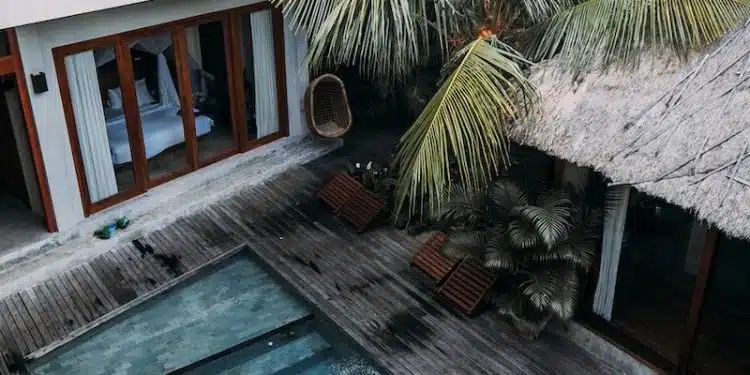 From above of wooden cottage with balcony located among tropical exotic trees with blue pool