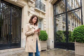 Jeune femme en trench beige devant un immeuble haussmannien